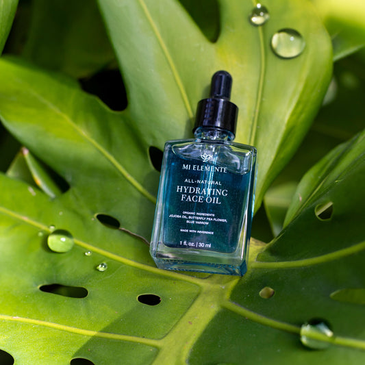 Blue bottle of face oil on a large green leaf with water droplets.